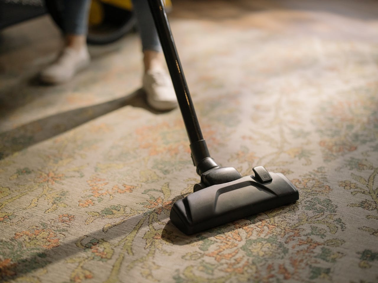 about-01 Close-up of a vacuum cleaner on a patterned carpet in a sunlit room, capturing a moment of household cleaning.